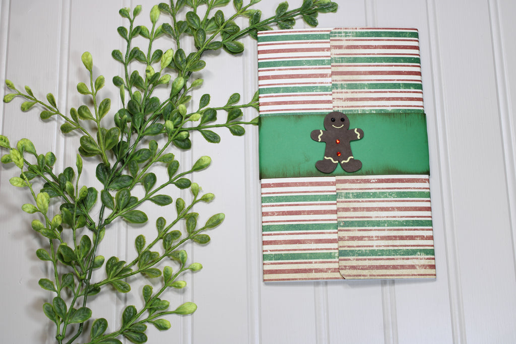 Notebook with gingerbread man design on a white wooden surface with green leaves.