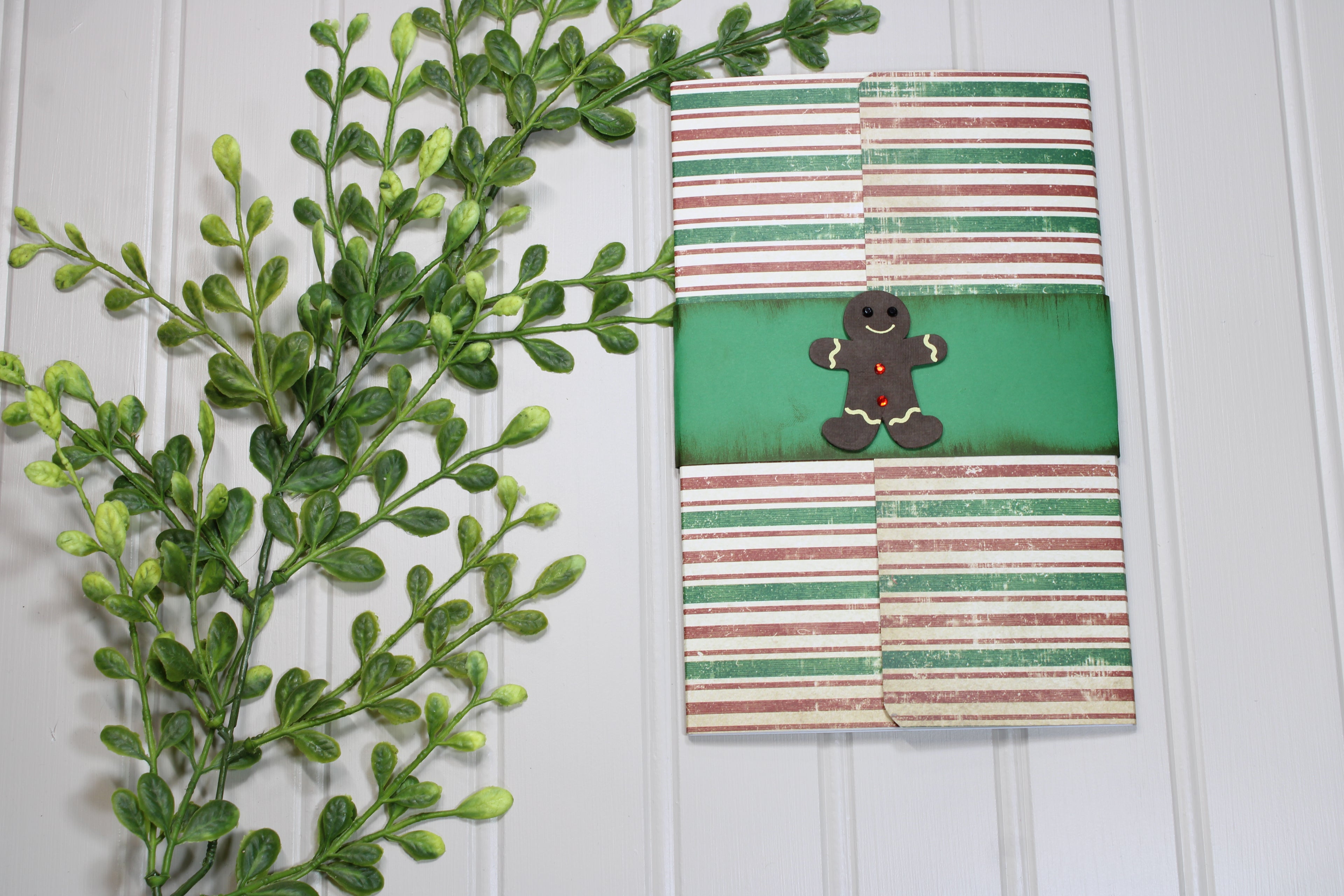 Notebook with gingerbread man design on a white wooden surface with green leaves.